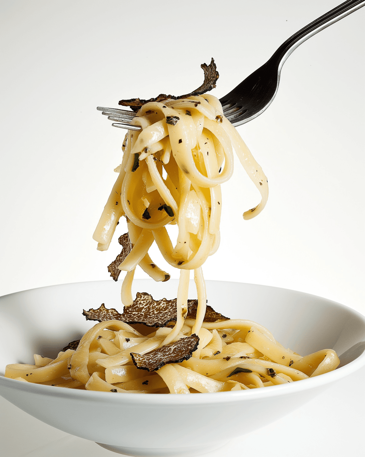 A fork lifting ribbons of fresh pasta with black truffle out of a white bowl